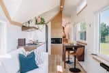 Interior of Fritz Tiny Home MacDonald model with light wood floors, white ceiling and white walls, medium-toned millwork, lofted bedroom, white kitchen cabinets, and dark wood countertops.