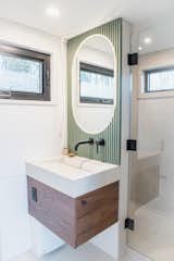 Interior of Fritz Tiny Home Halcyon model with white walls, wall-mounted sink vanity, and rounded mirror set into green millwork and backlit by LED lighting.