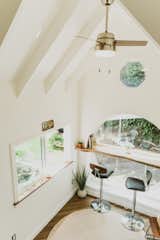 Paradise Tiny Home's Oasis model with white walls, sharply gabled ceiling with exposed beams, mango wood bar placed at middle of 6-foot wide circular window, and tall metal bar chairs upholstered in black leather in Hawaii Hawai'i.