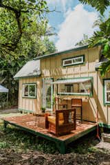 Paradis Tiny Home's Oasis model with yellow beige exterior paint with green window trim, long kitchen window that opens onto outdoor bar on porch in tropical forest in Hawaii.