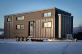 Minimaliste prefab tiny mobile home charme model with dark cedar and standing seam metal siding sits parked in a snowy field.