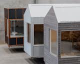 Three ROAM tiny mobile homes on a three-axle trailers by Fabprefab stand in line. One tiny home is clad in blackened Weathertex siding, the second tiny home is cladded in light zincalum sheets, and the third tiny home is clad with grey Accoya timber lap siding.