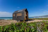 Tiny home by Madeiguincho with blackened cladding and large skylight sits on a trailer on rocky beach.