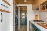 Interior of Summit Tiny Homes Nysos model with Oak ceiling and overhead cupboards, white Corian countertops, ceramic backsplash, and dark green cabinetry.