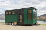 Summit Tiny Homes Nysos Model with blackened wood and green metal siding cladding sits on a road overlooking rolling landscape.