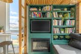 Interior of Summit Tiny Homes Nysos model with dark green millwork shelving library unit with compartments for television screen and fireplace beneath lofted sleeping area.