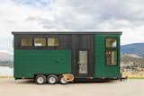 Summit Tiny Homes Nysos Model with blackened wood and green metal siding cladding sits on a road overlooking rolling landscape.