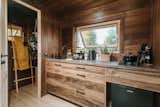 The kitchenof Vagabond Haven's prefab tiny called Nature Pod with pine floors and walls, Thermowood cabinetry, gas range, and kitchenware arranged beneath an awning window.