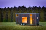 ESCAPE homes prefab tiny home ONE model with blackened yakisugi shou sugi ban vertical cladding sits on trailer in a grassy field.