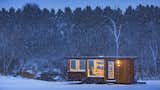 Man works at table inside ESCAPE homes prefab tiny home vista model with vertical wood cladding sits on a trailer in a snowy field.