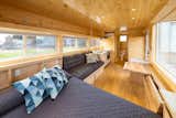 Interior of ESCAPE homes prefab tiny home vista boho model with pine wood finished interior, bed with dark blue grey coverlet, charcoal grey couch with wood storage beneath it, and inbuilt fold-up tables built into walls.