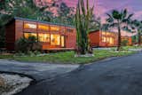 ESCAPE homes prefab tiny home traveler model with red horizontal wood cladding, deck, clerestory windows and shed roof sit in a row on a verdant street in Tampa Bay, FL, U.S.A.