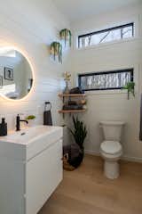 Zook Cabins and New Frontiers Design made the Luna Park Model Tiny Home with white shiplap walls and ceiling, light engineered hardwood floors, and bathroom whit white floating, wall-mounted vanity, round mirror with LED lighting, white planters along the walls, and corner, wall-mounted oak shelves carrying towels.