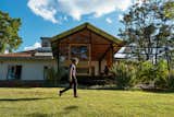Man walks on grassy lawn of extension to a home in Nairobi, Kenya, designed by Studio Propolis, co-founded by Naeem Biviji and Benthan Rayner, with gable roof, floor-to-ceiling glass windows, and large, wood-framed, sliding glass door that opens onto backyard.