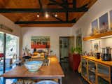 Kitchen in home in Nairobi, Kenya, designed by Studio Propolis, cofounded by Naeem Biviji and Benthan Rayner, with long metal-framed and medium-toned wood toped kitchen island and cabinetry with fluted glass doors, exposed metal beams with shed-style paneled wood ceiling.