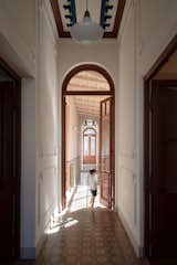 Boy opens up glass paned door with red-brown trim in tall hallway of home in the old quarter of San Antonio de Areco, Argentina, renovated by Julián Benedit Prebisch and Micaela Suide with geometric tile floors and white molding.