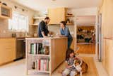 Heather Thompson, Sam Grady and their daughter spend time in their home kitchen in Portland, OR, renovated by Sill Design with kitchen island topped with white marble, grey tile backsplash, lightwood cabinetry, brown red countertops, overhead cabinets with textured glass sliding doors, and custom light-toned wood range hood.