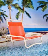 The Osan Leisure Chair by Ita with white metal folding frame and neon orange plastic seat and back photographed in front of sandbar with palm trees. 