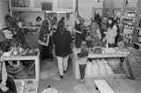 Spring fair in Kosmos by Gnomes, Amsterdam, The Netherlands, with young men and women talking and sorting among goods displayed on shelves and rustic wood tables.