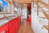 Interior of Honeylion tiny home by Modern Tiny Living with medium-toned wood vinyl flooring, bright red kitchen cabinetry, cubies built into staircase leading up to bedroom lofts, and white tongue-and-grove poplar finished walls.