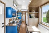Interior of Mi Casita tiny home by Modern Tiny Living with dark wood vinyl flooring, blue kitchen cabinetry, white walls, dark maple millwork units, and lofted bedroom.