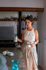 Woman pours coffee into small china cups from moka pot in the kitchen with a green brown stone island and white ceramic porcelain backsplash, and kitchen utilities set into a long nook in the wall in a home in Lanzarote, Canary Islands, Spain, renovated by Patricia Betancourt Ramos.