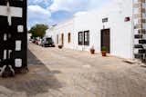 A home in Lanzarote, Canary Islands, Spain, renovated by Patricia Betancourt Ramos with white stucco façade and medium-toned wood old antique doors, wood window frames, and wood shutters sits on paved street.