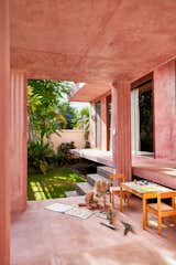 A girl draws beside a short, small table in a pink open-sided concrete room with grooved columns beside a grassy, verdant courtyard in a house in Bali designed by Los Angeles–based Ham Design Group, led by Keith and architect Corie Saxman.