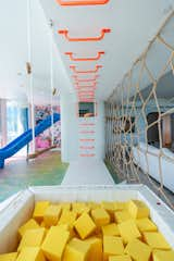 A kids’ space designed by Smart Playrooms for a client features monkey bars, a slide, and a swing above a foam pit, separated from the living room by a rope "spider web" wall.