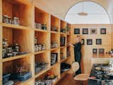 Woman sorts through objects stowed in wall-to-wall millwork cabinetry installed in an art studio with arched curving roof built on a flatbed trailer in Salida, CO, with arched clerestory window and disk pendant lights.