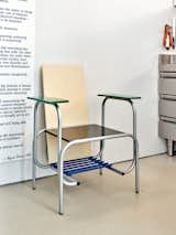 Metal armchair with black seat, green arm rests, blue storage tray beneath seat, and beige back rest in an apartment in Madrid, Spain, renovated by architect Eduardo Mediero.