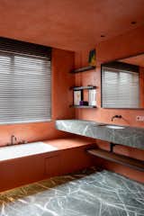 Bathroom in an apartment in a mixed-used building in Ghent, Belgium, designed by Jeremy Godenir, founder of MOEA Architectural Design Studio with orange walls and ceilings and grey stone floors and counters and floating vanity.
