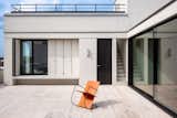 Sculptural orange armchair stand on terrace of an apartment in a mixed-used building in Ghent, Belgium, designed by Jeremy Godenir, founder of MOEA Architectural Design Studio with floor-to-ceiling glass doors, a narrow concrete staircase leading up to rooftop terrace.