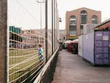 Alleyway between soccer field and shipping containers leads to brick factory converted into an apartment by Gabriele Schiavon, creative director of Barcelona-based design studio Lagranja with tall arched windows.