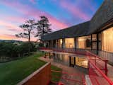 A deck with a bright red railing hugs the top level, while a wraparound stone patio awaits below.