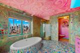 Vibrant color continues in the primary bedroom’s en suite bath, which has dual sinks, a glass-encased shower, and a tiled bathtub overlooking the skyline.&nbsp;