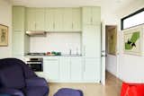 Kitchen in a 1960s A-frame with pastel green cabinetry, white tile backsplash, light wood flooring, and deep purple armchair and ottoman in Manhattan Beach, Los Angles, CA, renovated by Julie Anderson and Amy Dantzler in collaboration with architect Bryan Libit.