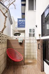 Terrace patio with concrete block walls, medium-toned wood gate separating deck with red wire chair from outdoor shower beside a 1960s A-frame in Manhattan Beach, Los Angles, CA, renovated by Julie Anderson and Amy Dantzler in collaboration with architect Bryan Libit.