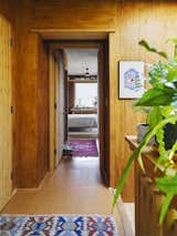 A hallway with cork flooring and medium-toned wood paneled walls and colorful rugs with geometric designs leads to bedroom with white area rug and bed with white bedspread in a house by architect Jack Becker and landscape architect Maddie Hoagland-Hanson in an alley in the Capitol Hill area of Washing-ton, D.C.