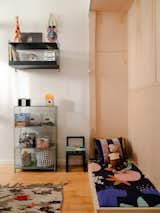Children's bedroom in Green Point, New York City, renovated by interior stylist and designer Merie Subryan with cream and white walls, low plywood bed with black blanket printed with large, cartoonish, colorful animals, doll of monkey curious George, green grey metal storage unit, and blue grey wall mounted metal shelving unit.