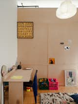 Office separated from children's bedroom by plywood partition in Green Point, New York City, renovated by interior stylist and designer Merie Subryan with translucent pendant light, plywood desk with blue chair, and cartons with toys.