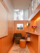 Office with plywood interior, white board, velvet green armchair, brown stool ottoman, high polycarbonate clerestory windows, built-in storage, round flat green wall light sconce, accent lighting, and raised desk in work shed by Linework Architecture in backyard of home in Seattle, Washington.