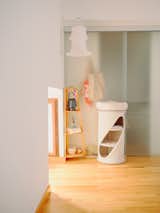 Bedroom in a tiny seaside home for Massimo Ricci and Valentina Martinelli in Termoli, Italy, renovated by Rispoli Guerrera Architetti with light hardwood floors, white floral tulip pendant light, white fabric cylinder with three tiered round beds for cats, closet covered with translucent doors, tiered wood corner end table, and white walls. 