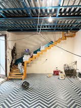 Photographed during construction, a yellow staircase steps up from a living room with blue-and-white herringbone tiles and ceiling with exposed blue metal beams in a tiny seaside home for Massimo Ricci and Valentina Martinelli in Termoli, Italy, renovated by Rispoli Guerrera Architetti.