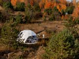 Family walks through tall grass outside geodesic dome by FDomes with an interior designed and built by SpotLab in Lost Woods glamping sloping forested site situated in Boyne Falls, Northern Michigan.