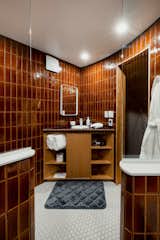 Bathroom with hexagon white ceramic tile floor, burnt orange porcelain tile walls, and triangular oak vanity with black tile top in a geodesic dome by FDomes with an interior designed and built by SpotLab in Lost Woods glamping site situated in Boyne Falls, Northern Michigan.