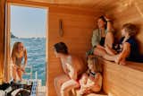 Family sit together inside floating sauna clad in cedar and hemlock wood slats designed and built by Peter Boldt as it sails off the coast of Cos Cob, Connecticut.