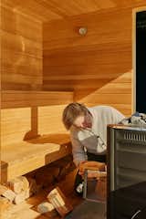 Man stokes wood-burning stove in floating sauna clad in cedar and hemlock wood slats designed and built by Peter Boldt  as it sails off the coast of Cos Cob, Connecticut.