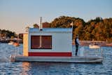 Man sails floating sauna clad in red-and-white wood slats designed and built by Peter Boldt off the coast of Cos Cob, Connecticut.