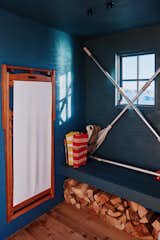 Cabin of floating sauna clad in red-and-white wood slats designed and built by Peter Boldt with dark turquoise walls, long bench with chopped firewood stowed beneath, black wire basket filled with towels, metal oars, and wood plank flooring.
